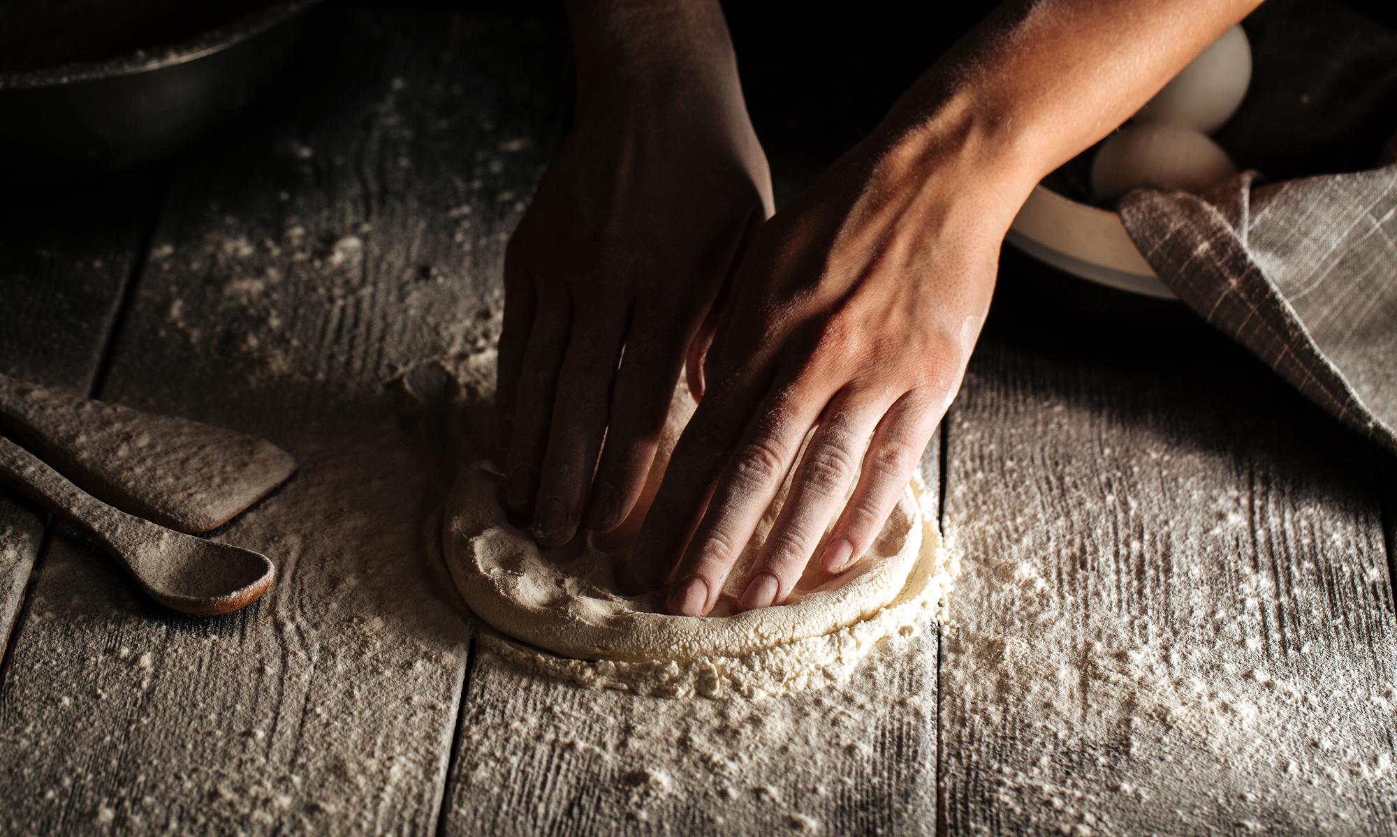 hands kneading dough on wooden table